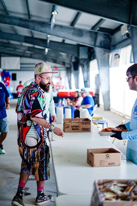Volunteer handing out boxes at an indoor relief center, with people lined up in the background