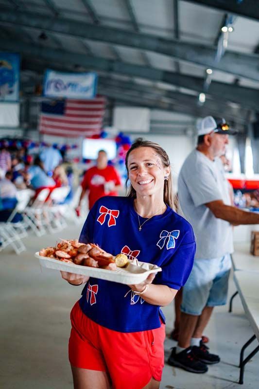 Smiling server in blue shirt and red shorts carrying a plate of food in a busy indoor venue
