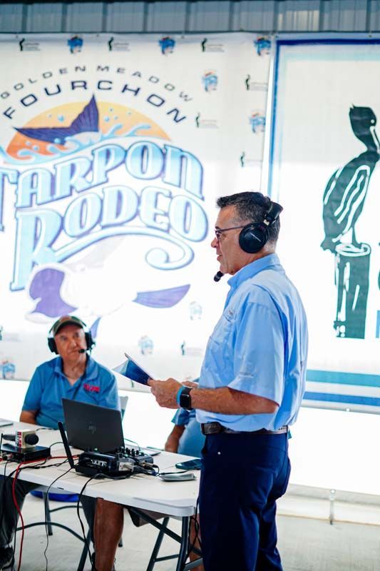 Man speaking into a headset beside a seated technician at a Tarpon Rodeo event booth