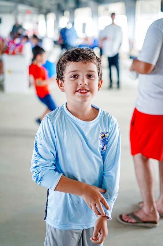 Young child in a light blue shirt smiling in a busy indoor hallway