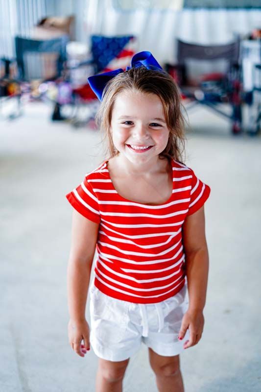 Smiling child in a red striped shirt and white shorts standing indoors