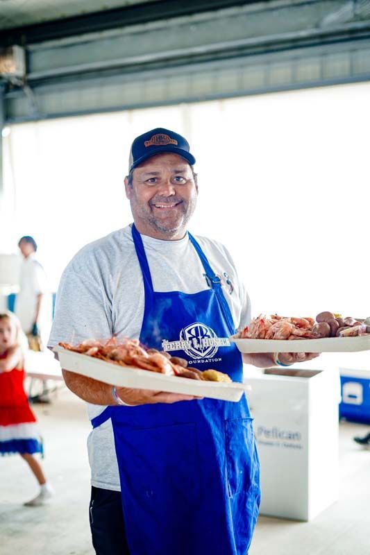 Man in blue apron and cap holding trays of baked goods at an indoor market stall