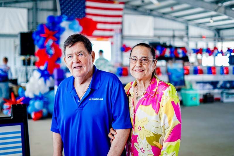 Two people in blue and pink shirts stand in a store decorated with red, white, and blue balloons and an American flag