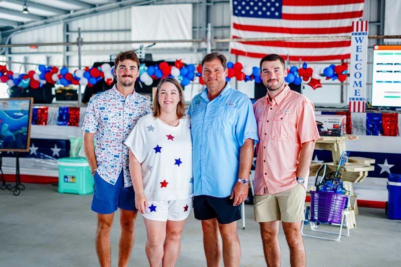 Four people posing in a decorated indoor space with red, white, and blue bunting and an American flag overhead