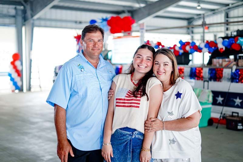 Three people smiling in a decorated indoor venue with red, white, and blue patriotic decor