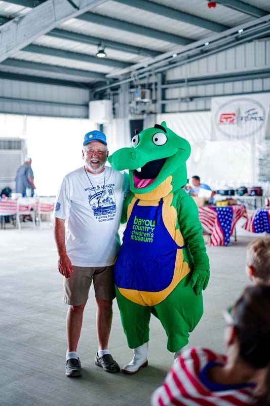 Man posing with a green mascot in a blue vest inside a bright indoor event hall