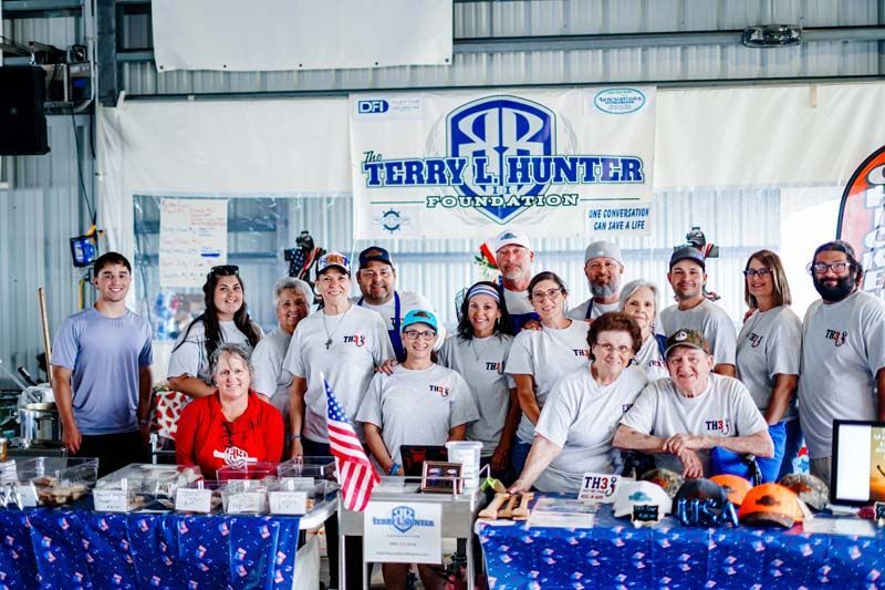 Group of people at a Terry Hunter booth with banners, trophies, and small American flags at an indoor event