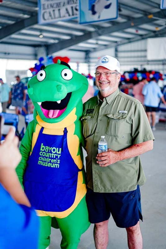 Man in green shirt posing with a green mascot in a blue-and-yellow jersey at an indoor event
