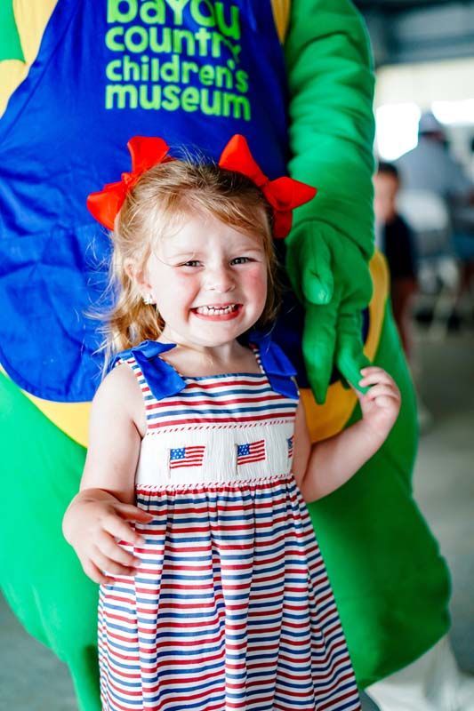 Smiling child in a red, white, and blue dress standing with an adult in a green costume