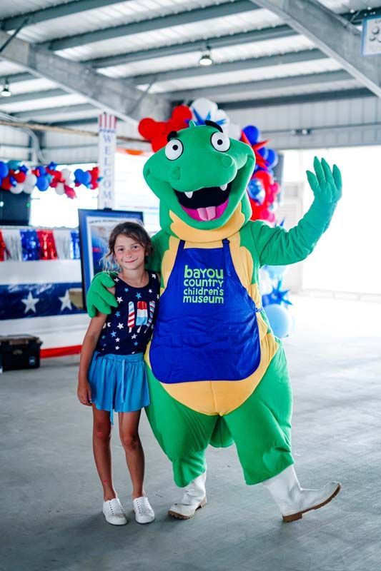 Girl posing with a green mascot in a blue apron, waving inside an ice rink