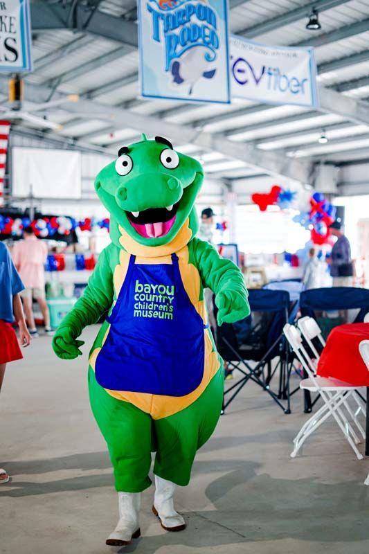 Green mascot in a blue apron walking indoors at an event venue