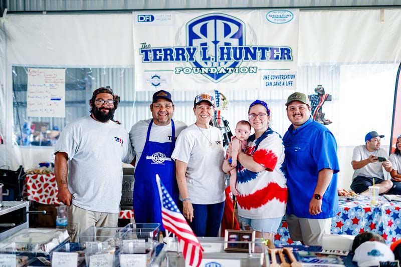 Five people stand behind a table at a Terry L. Hunter campaign event, holding an American flag.
