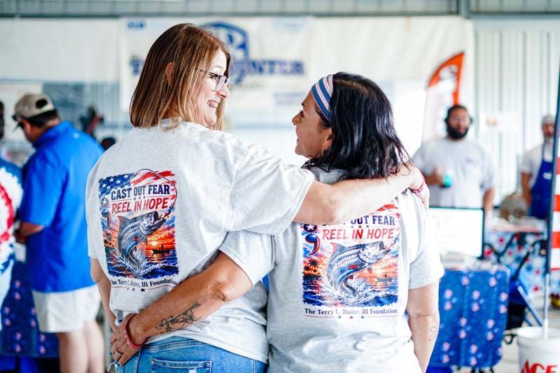 Two people in white event T-shirts embrace at a busy indoor gathering