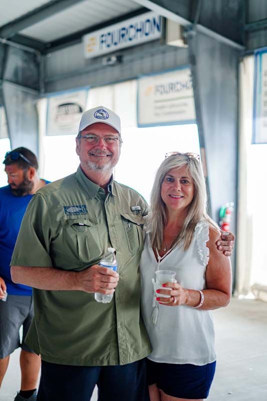 Two smiling adults holding drinks in a casual indoor venue, standing under a “Fourchon” sign.