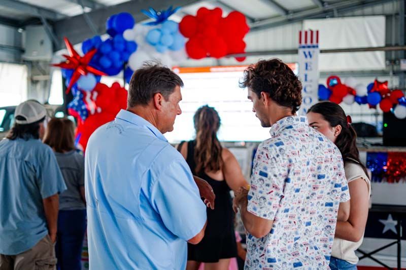 People chatting at a decorated indoor event with red, white, and blue balloons