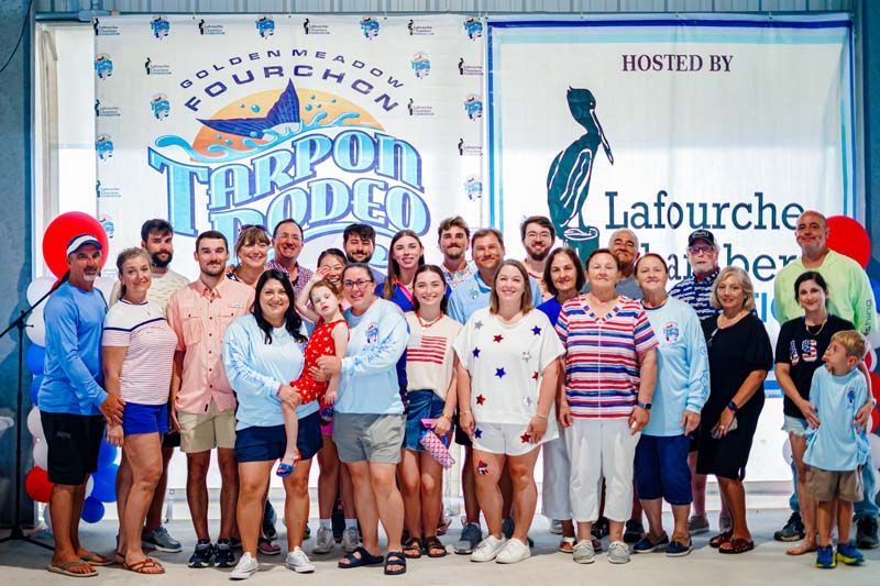 Group of people posing at a Tarpon Rodeo event banner with Lafourche Parish logo behind them