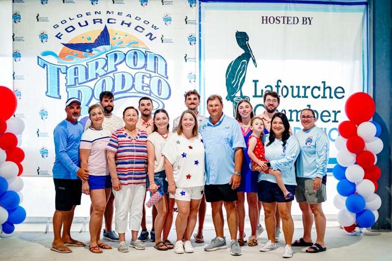 Group posing at a Tarpon Rodeo event booth with red, white, and blue balloon columns