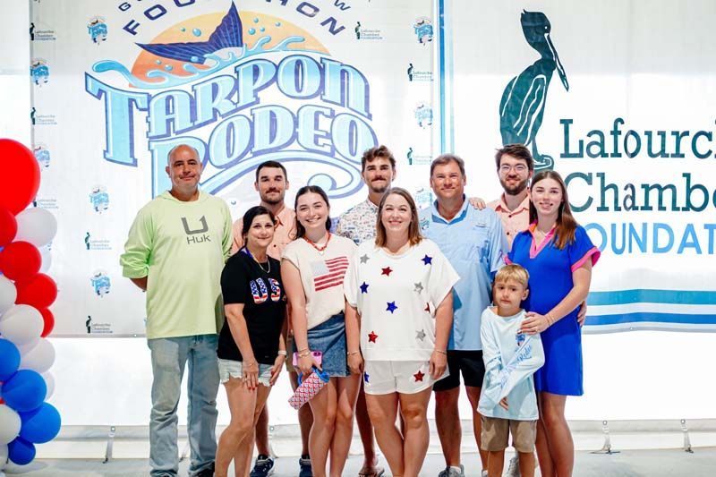Group of people posing in front of a “Tarpon Rodeo” and Lafourche Chamber Foundation banner with balloons