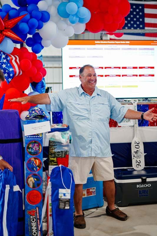 Man smiling at a trade show booth with red, blue, and white balloon decorations and display items