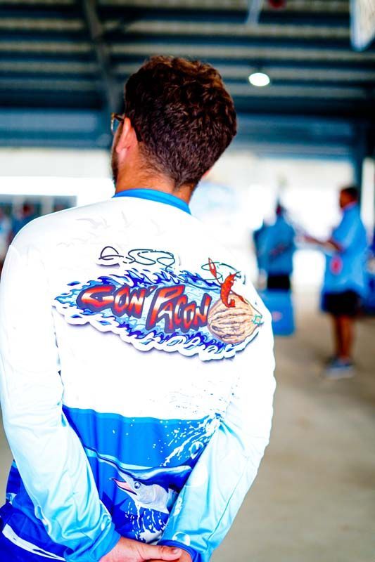 Person in a white-and-blue jersey with a graphic back design, standing with hands behind their back indoors.
