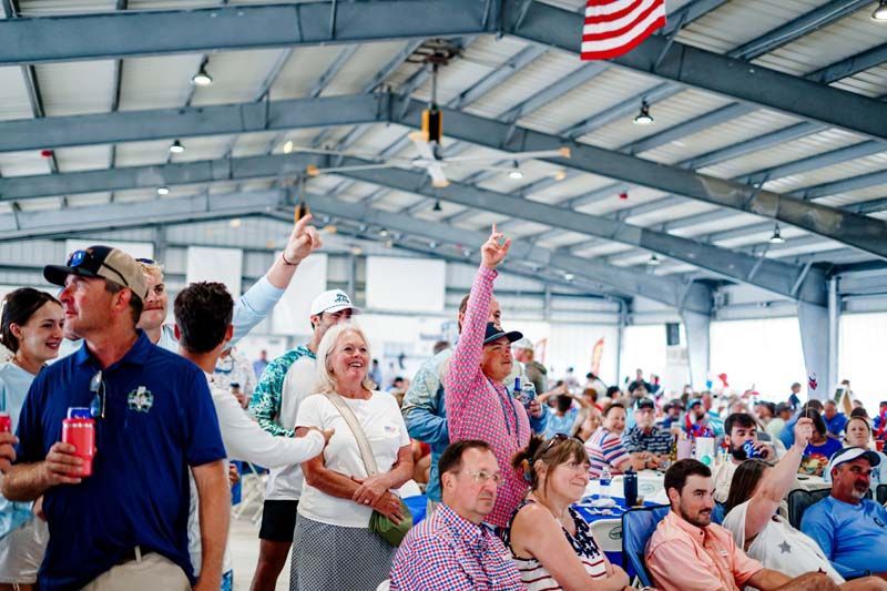 Crowd cheering under a pavilion, with people raising hands and a U.S. flag overhead