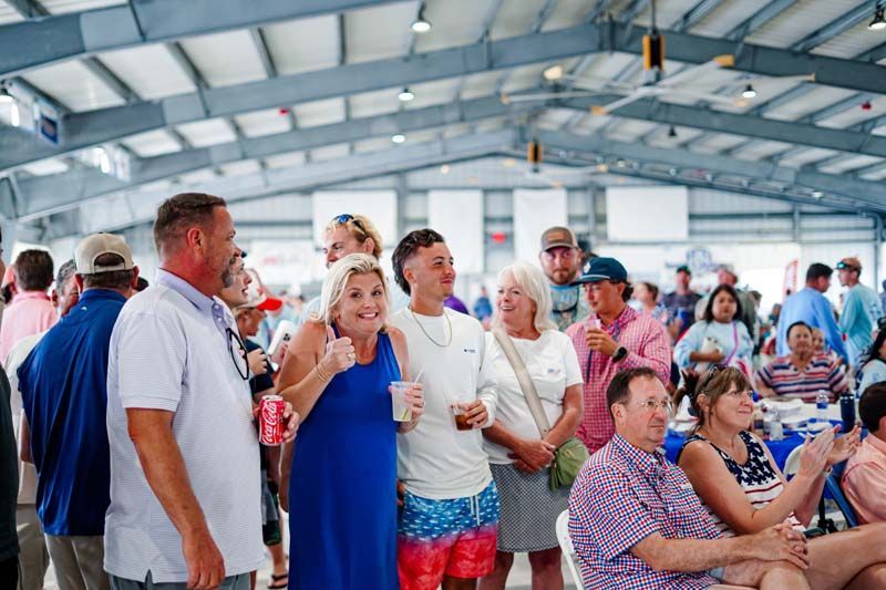 Crowd gathered under a metal pavilion, chatting and eating at a casual outdoor event