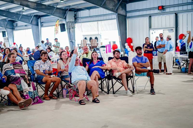 People seated on folding chairs in a large indoor hall during a community event