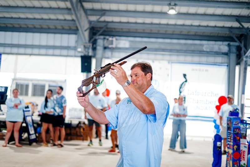 Man aiming a shotgun at an indoor shooting range, with people watching in the background