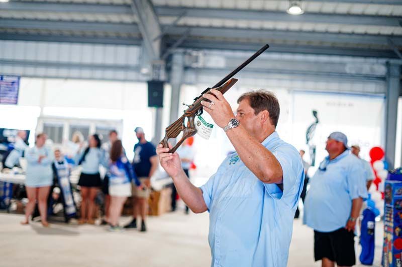 Man in a light blue shirt aiming a rifle at an indoor shooting range