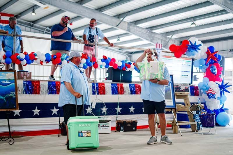 Two speakers at a patriotic-decorated stage with red, white, and blue balloons in a covered venue