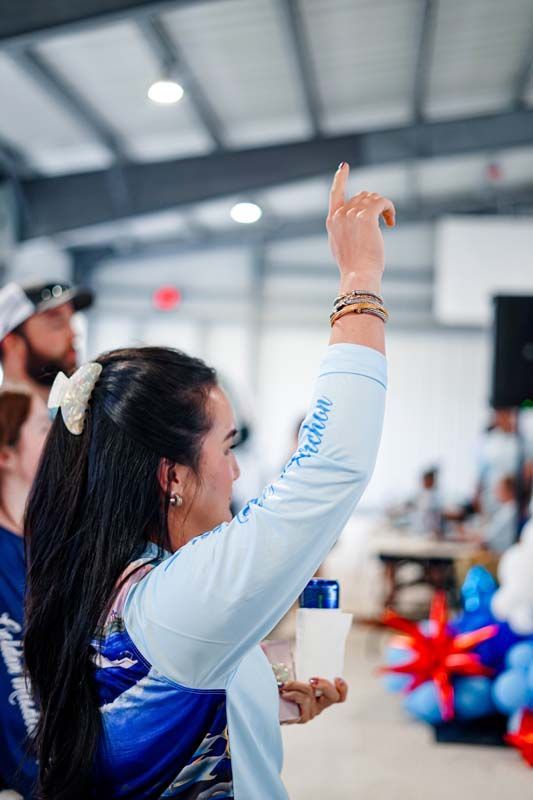 Woman in white and blue shirt raises hand at an indoor event