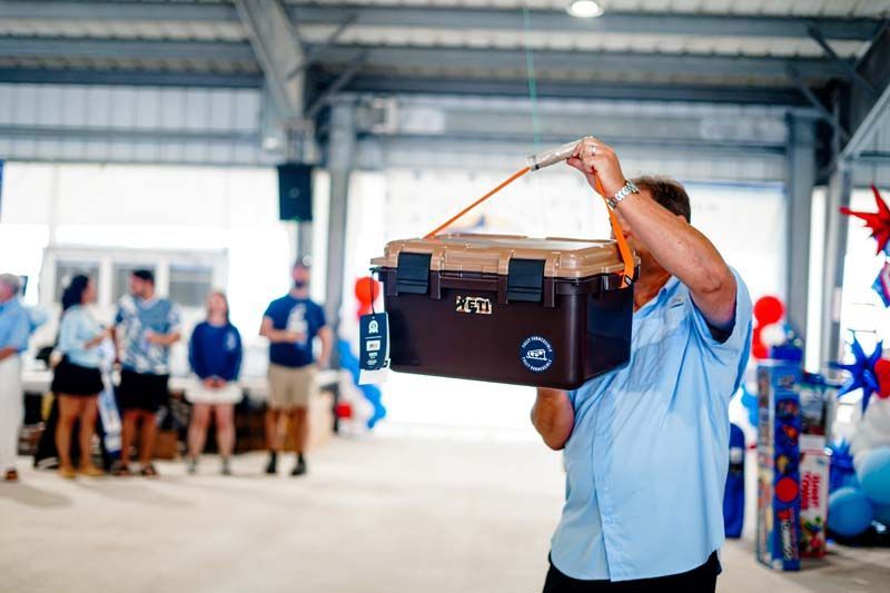 Man lifting a black speaker box in a bright indoor event hall with people standing in the background