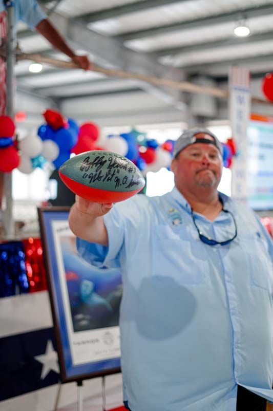 Person holding out a signed football at an indoor event with red, white, and blue decorations