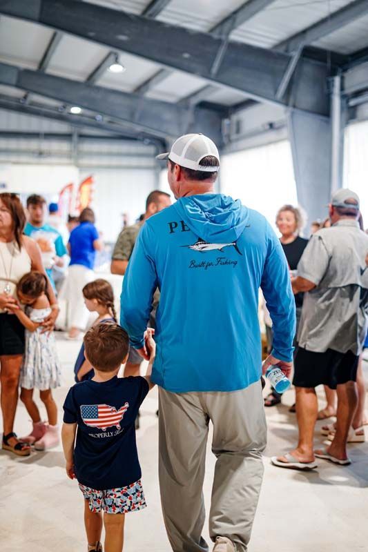 Man in blue hoodie holding a child’s hand in a crowded indoor hall