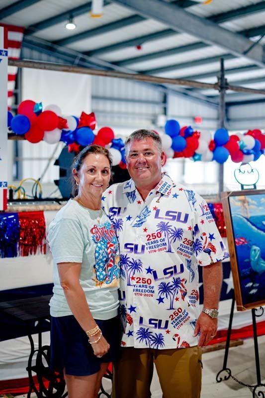 Two people smiling at an LSU-themed event with red, white, and blue balloon decorations.