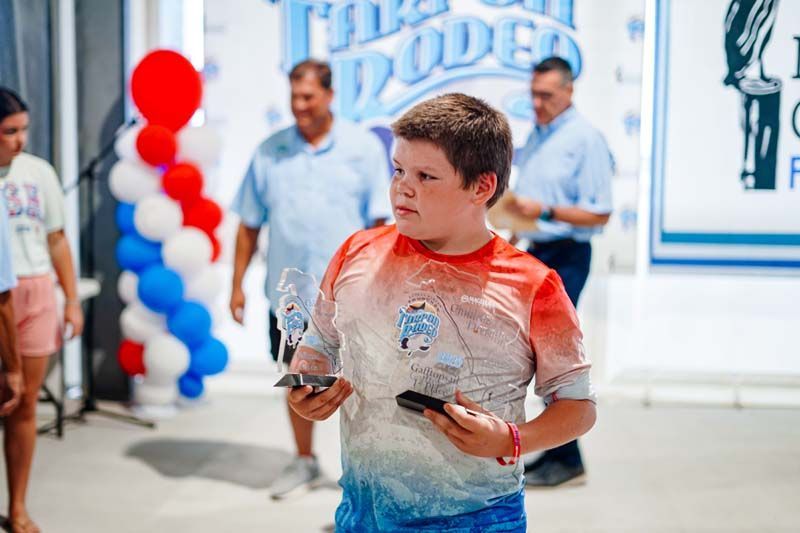Child in red, white, and blue shirt holding an object at a festive event with balloon decorations