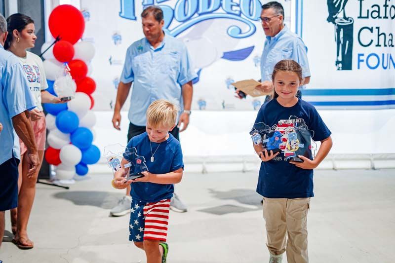 Children holding red, white, and blue balloon bouquets at a charity event backdrop