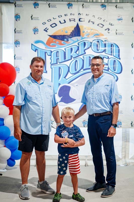 Three people posing in front of a “Luau Pockets” banner, with red balloons beside them.