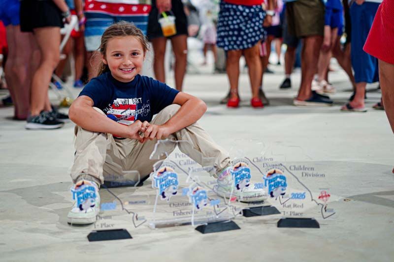 Child kneeling beside a row of small decorated shoes on a street, with people standing in the background