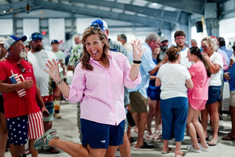 Woman in pink shirt waving in a crowded indoor event space.