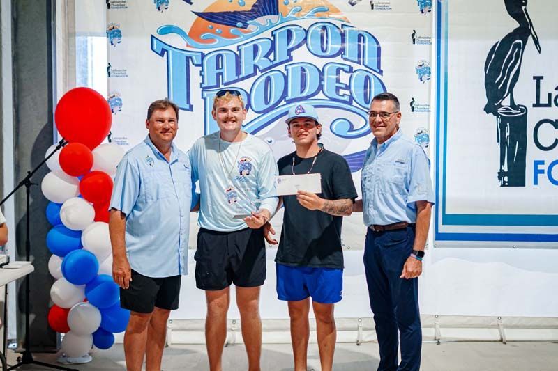 Four men posing at a Tarpon Lodge event, with red, white, and blue balloons nearby