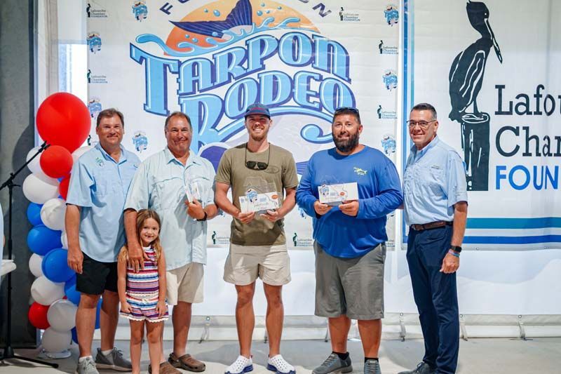 People posing with a trophy and red balloon at a Tharpon Thoden charity event banner.