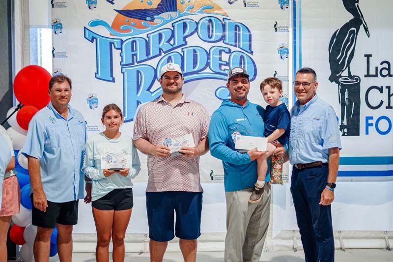 Six people posing with plaques in front of a Tarpon Rodeo sign at an event booth