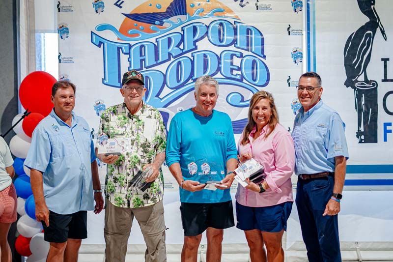 Five people stand in front of a “Tarpon Rodeo” sign, smiling and holding an award.