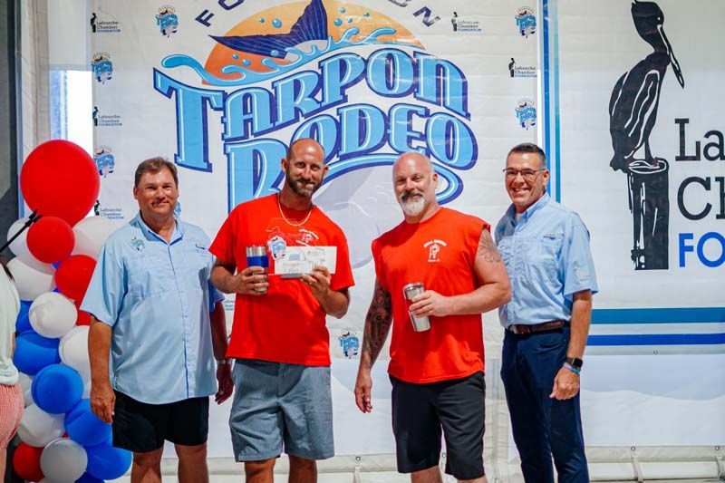 Four men pose with a certificate at Tarpon Rodeo, in front of event banners.