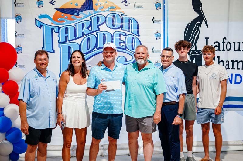 Seven people posing in front of a large “Harpoon Hoods” sign, smiling at an indoor event.