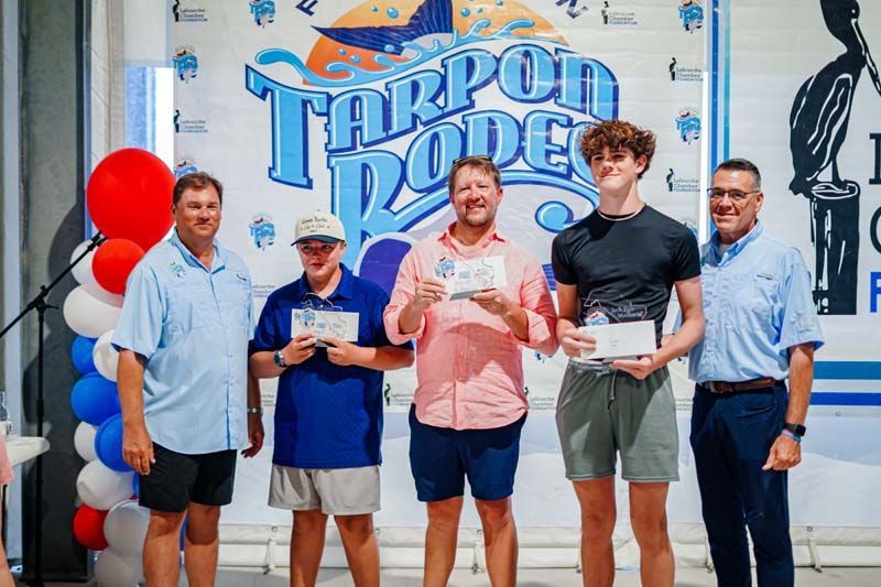 Five people holding awards stand in front of a Tarpon Lodge mural, with balloons at the left.