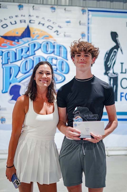 Two people stand in front of a “Harpoon” banner, holding an award plaque and smiling.