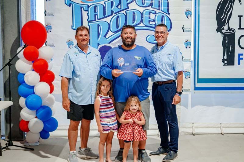 Group posing in front of a blue Tarpon Rodeo sign with red, white, and blue balloons