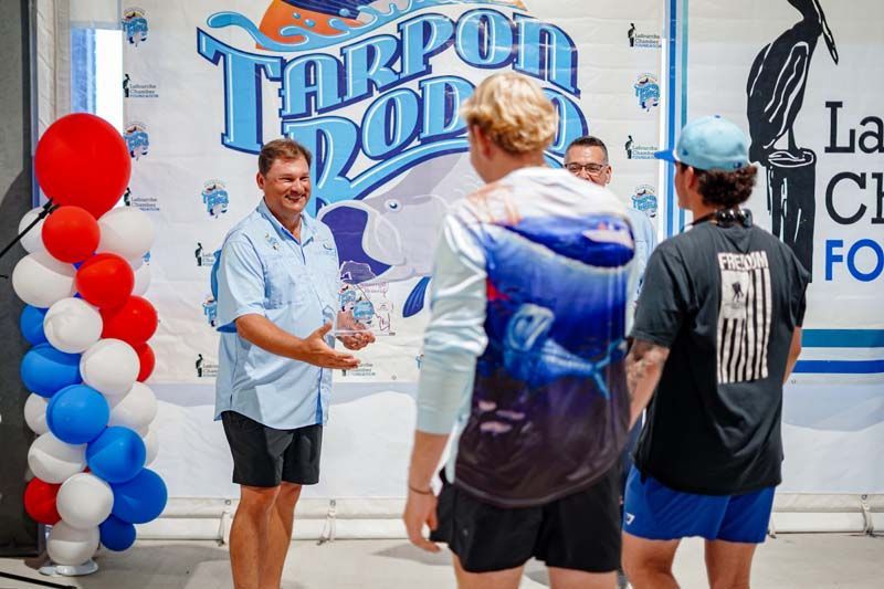 People chatting at a Tarpon Rodeo booth beside red, white, and blue balloon decorations.